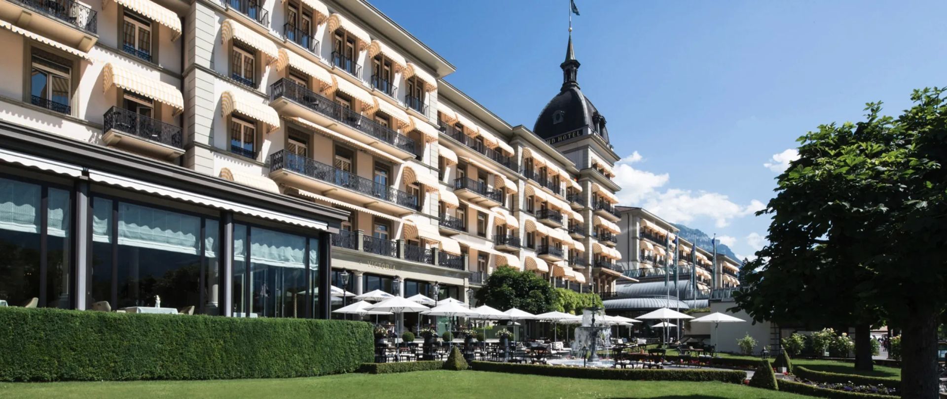 Luxushotel mit weitläufigem Garten und sonniger Terrasse vor alpinem Hintergrund