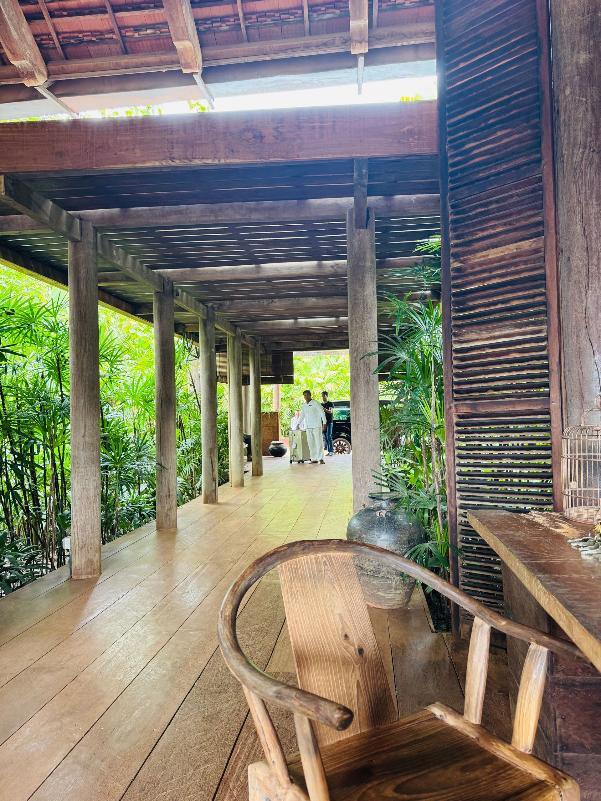 Offene Veranda aus dunklem Holz mit geflochtenem Stuhl, dahinter der Blick in den Garten
