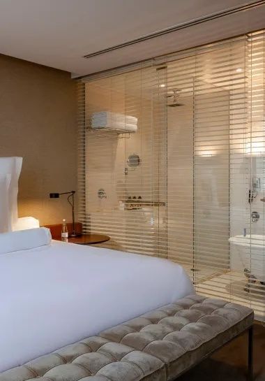 Modernes Hotelzimmer mit Bett und durchsichtiger Glaswand zum Badezimmer.