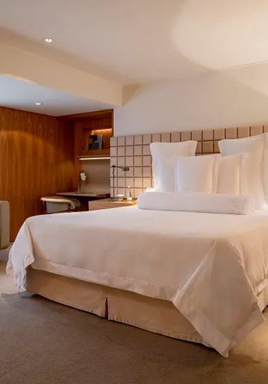 Hotelzimmer mit weiß bezogenem Doppelbett und Schreibtisch im Hintergrund