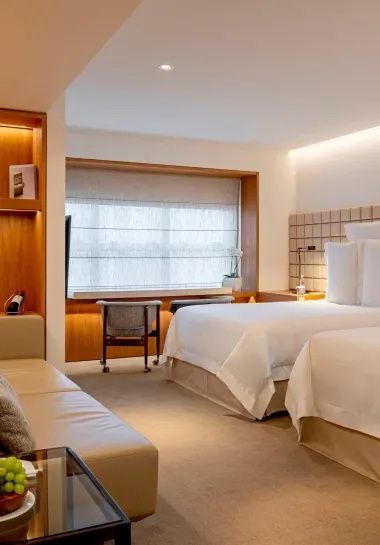 Hell eingerichtetes Hotelzimmer mit zwei Betten und einem Sofa