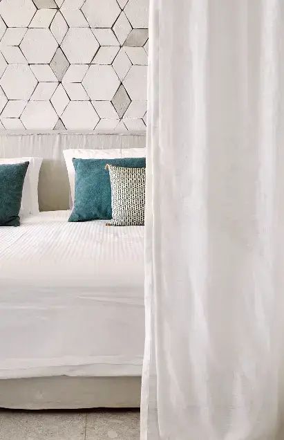 Doppelbett mit weißen Bezügen, grünen Kissen und gekachelter Kopfteilwand.