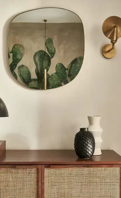 Holzkommode mit zwei Dekorationsvasen, Wandleuchte und Kaktusbild.