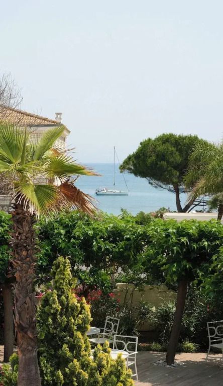 Meerblick vom Hotelgarten mit Palmen und Segelboot auf dem Wasser.