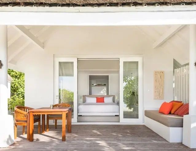 Holzterrasse einer Villa mit Esstisch, Stühlen und einer Sitzbank sowie Blick auf das Schlafzimmer.