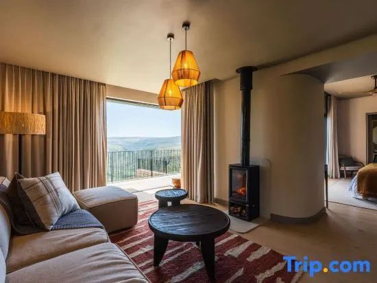 Wohnbereich mit Sofa, Kaminofen und Ausblick auf die umgebenden Hügel durch ein großes Fenster.