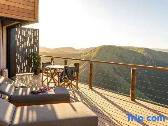 Holzterrasse mit Liegestühlen und Esstisch vor einer bergigen Landschaft im Abendlicht.