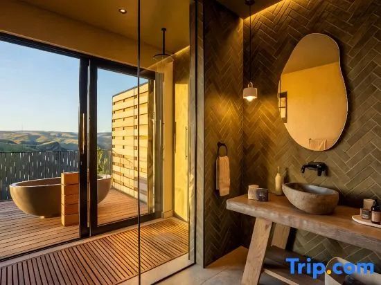 Badezimmer mit Holzwaschtisch, ovalem Spiegel und Dusche mit Zugang zur Außenterrasse.