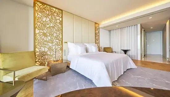 Hell eingerichtetes Hotelzimmer mit großem Doppelbett und vergoldetem Wandmuster.