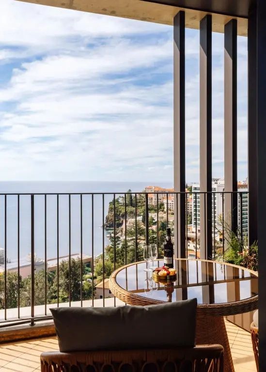 Balkon mit einem rundem Tisch und Blick auf die Küste mit Gebäuden und das Meer.