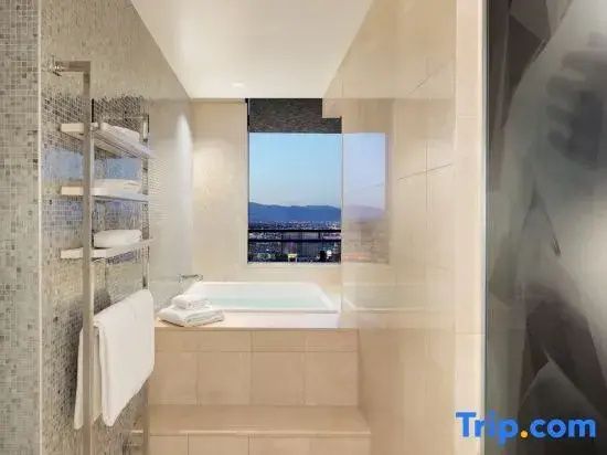 Badezimmer mit eingebauter Badewanne vor einem Fenster mit Aussicht auf die Stadt.