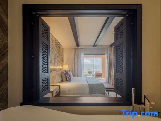 Blick durch ein Holzfenster auf ein Doppelbett mit hellen Kissen und Balkonzugang.