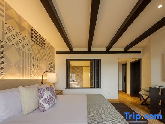 Doppelbett im Hotelzimmer mit gemustertem Kopfteil und Holzdeckenbalken.