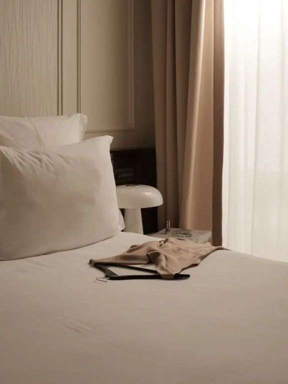 Gemütliches Bett mit beiger Tagesdecke und heller Vorhang