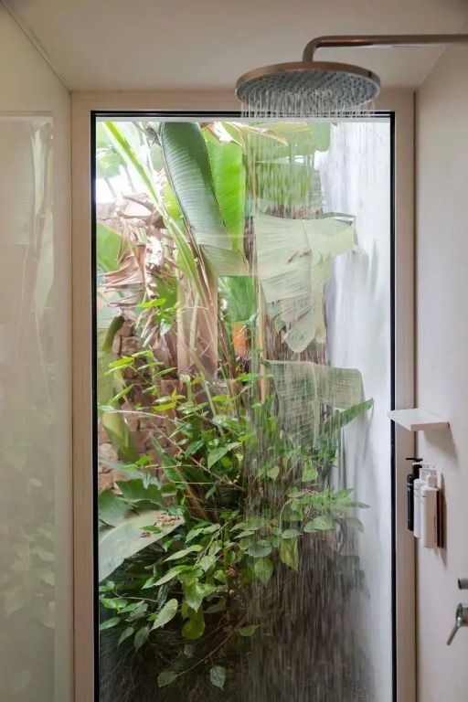 Badezimmerfenster mit Blick auf tropische Pflanzen und Wasserfall
