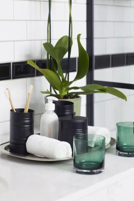 Moderne Badezimmereinrichtung mit Glasbechern, Pflanzen und Handtüchern.