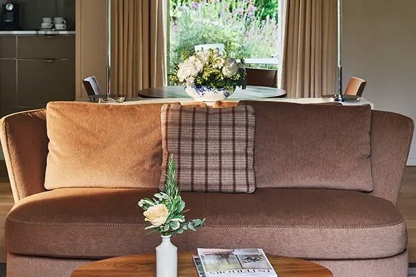 Sitzbereich mit braunem Sofa, Blumenvasen und einem runden Tisch am Fenster.