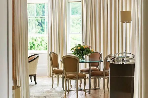 Heller Essbereich der Suite mit Glastisch und eleganten Stühlen vor einem großen Fenster