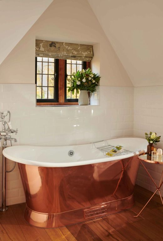 Elegante freistehende Badewanne mit Kupferoptik vor einem Fenster in einem stilvollen Badezimmer