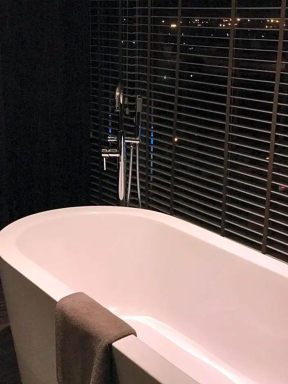 Moderne Badewanne im Badezimmer der Terrasse Suite mit Jalousien im Hintergrund