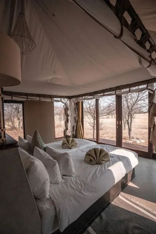 Innenansicht eines Premium Chalets mit Betten und Panoramafenstern zur Savanne
