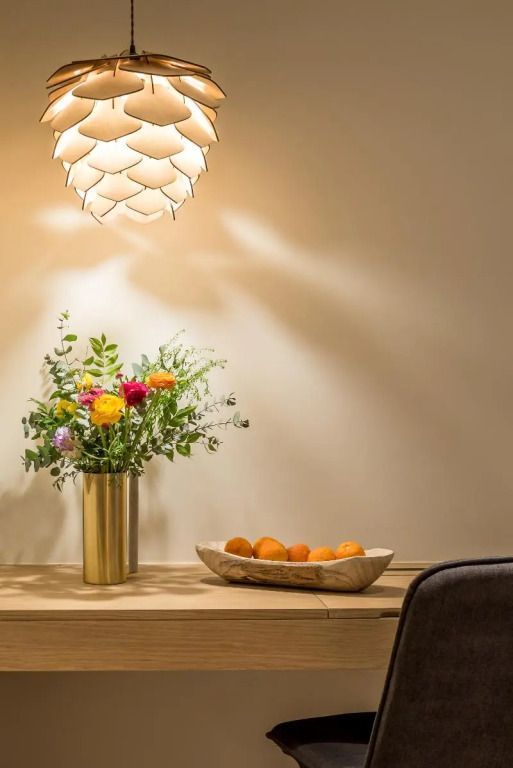 Vase mit Blumen und Obstschale auf einem Holzsideboard unter einer Designerlampe