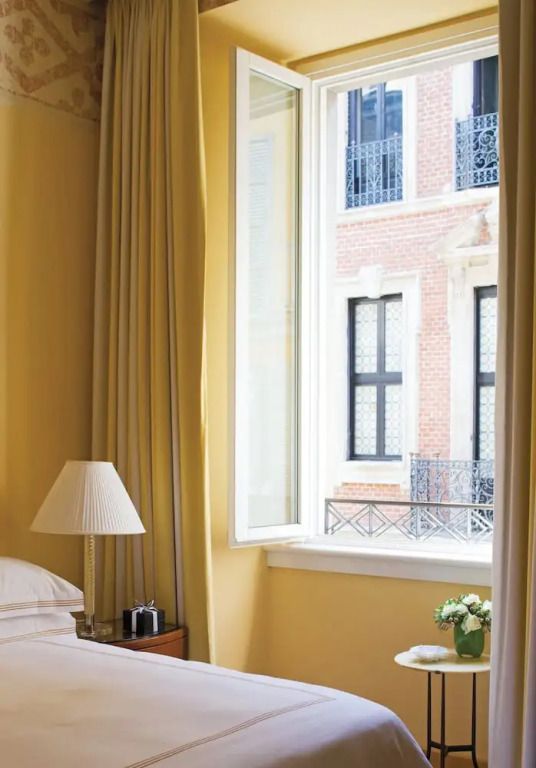 Gemütlicher Blick aus dem Fenster eines Hotelzimmers mit gelblichen Vorhängen und Ziegelbau.
