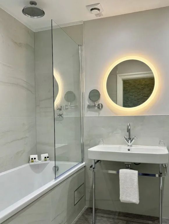 Modernes Badezimmer mit beleuchtetem Rundspiegel und eleganter Badewanne