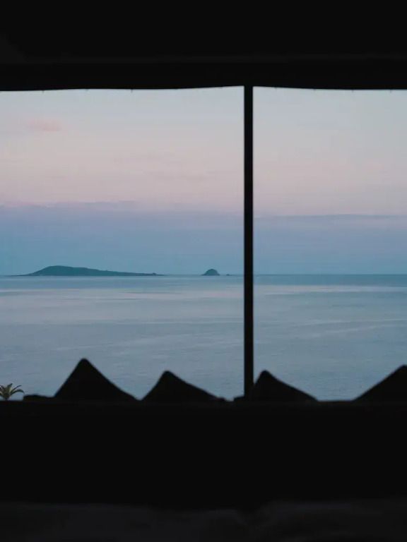 Blick aus dem Zimmerfenster auf das weite Meer und Inseln bei Dämmerung