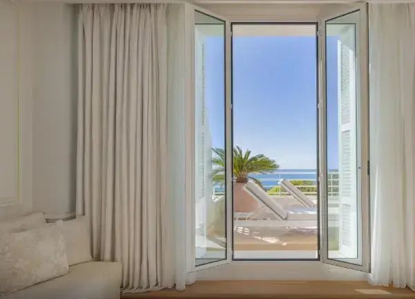 Offene Fensterfront zur Terrasse mit Meerblick und Sonnenliegen