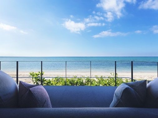 Blick von der Terrasse auf den Strand und das blaue Meer unter klarem Himmel.