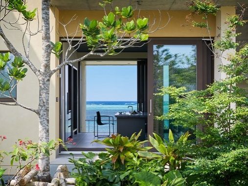 Terrasse mit Sitzgelegenheit und Blick auf grüne Pflanzen und das Meer