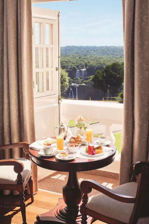 Frühstückstisch auf Balkon mit Aussicht auf Wasserfälle und üppige Natur.