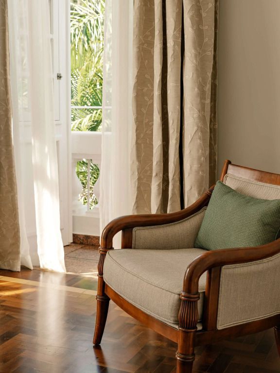 Komfortabler Sessel mit einem Kissen neben einem Fenster mit Vorhängen.