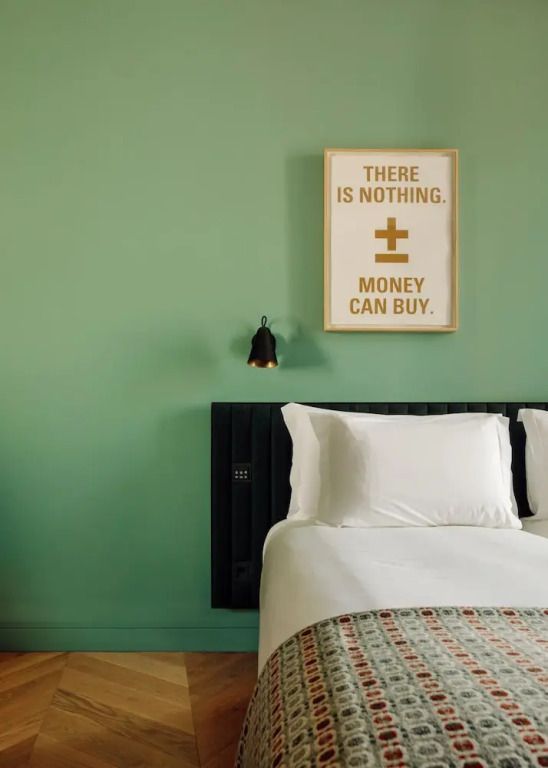 Zimmerdetail mit Bett und moderner Kunst an einer grünen Wand.