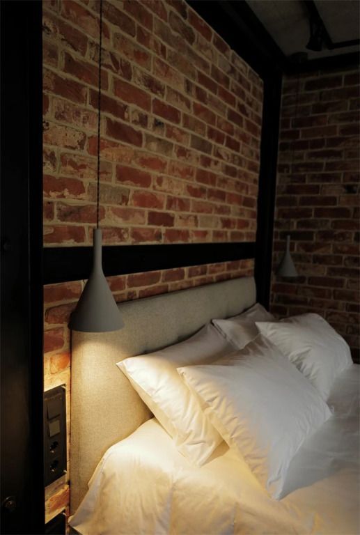 Moderne Nachttischlampe an Backsteinwand über dem Bett