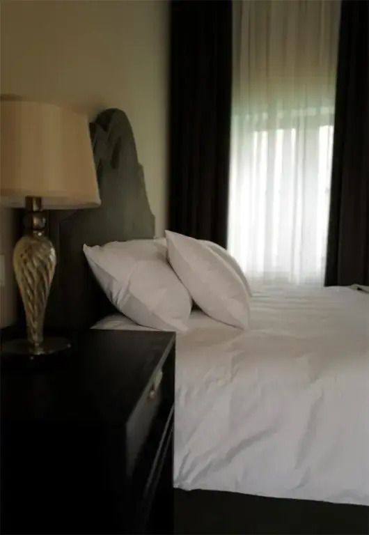 Elegantes Doppelbett mit weißen Kissen und stilvoller Lampe in modernem Zimmer