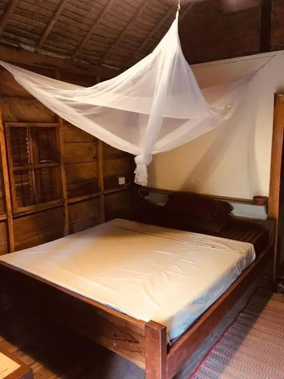 Bungalow-Innenraum mit großem Bett und Moskitonetz unter einem Strohdach