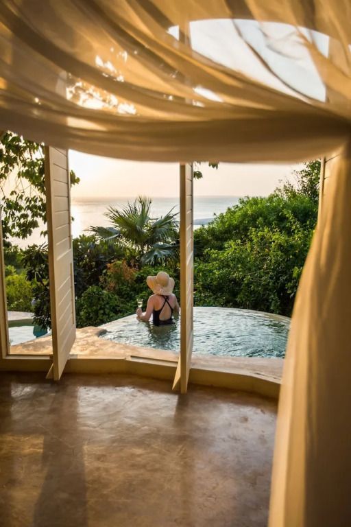 Frau im Infinity Pool mit Blick auf den Ozean bei Sonnenuntergang