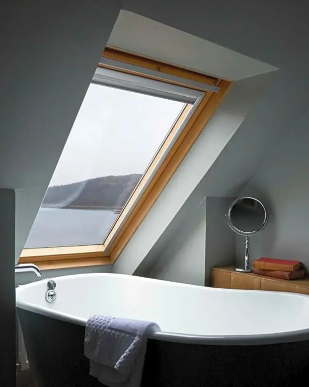 Luxuriöses Badezimmer mit freistehender Badewanne und Dachfenster mit Seeblick
