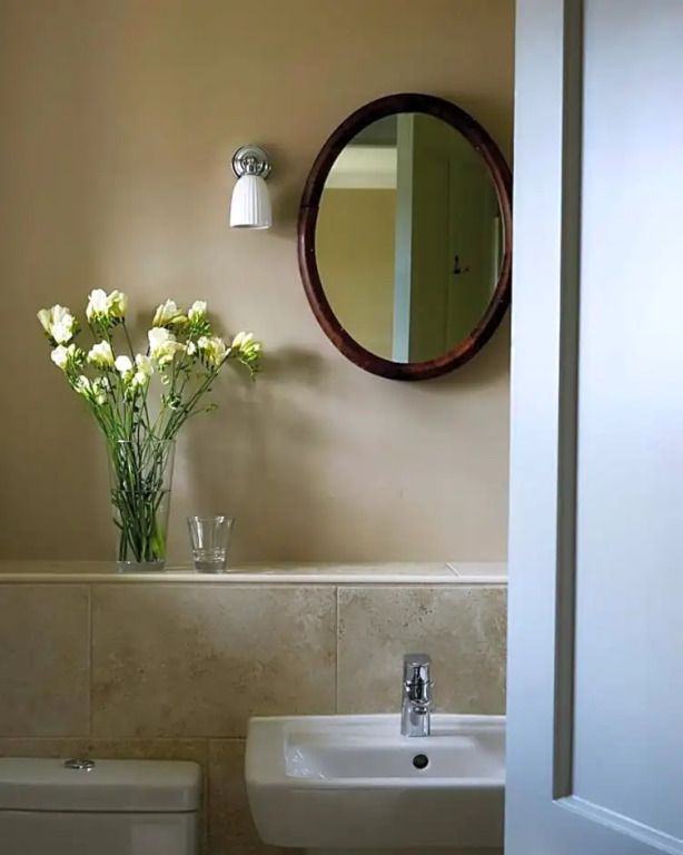 Elegantes Badezimmer mit rundem Spiegel und frischen Blumen im Glasgefäß.
