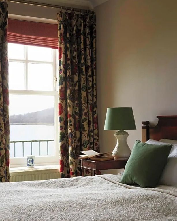 Doppelzimmer mit Meerblick, grüne Lampe und florale Vorhänge bei offenem Fenster.