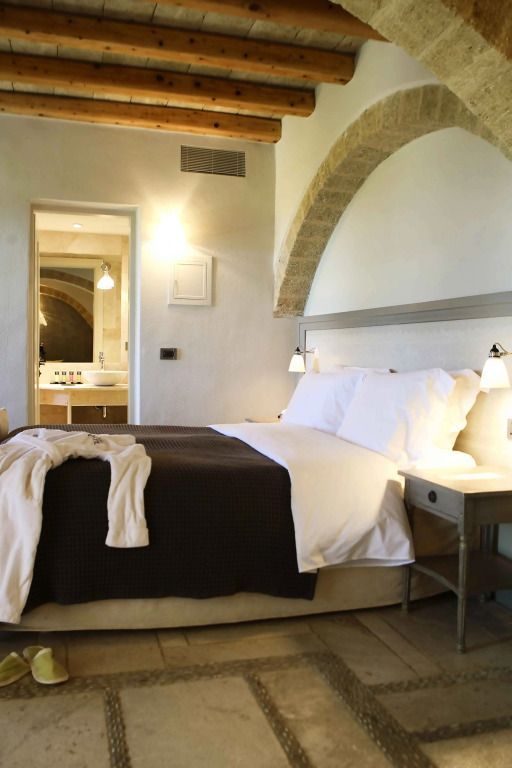 Helles Schlafzimmer mit großem Bett und Tagesdecke in einer Junior-Suite mit Blick ins Bad.