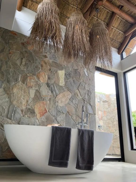 Freistehende Badewanne in Natursteinbad mit Strohdach im Badezimmer
