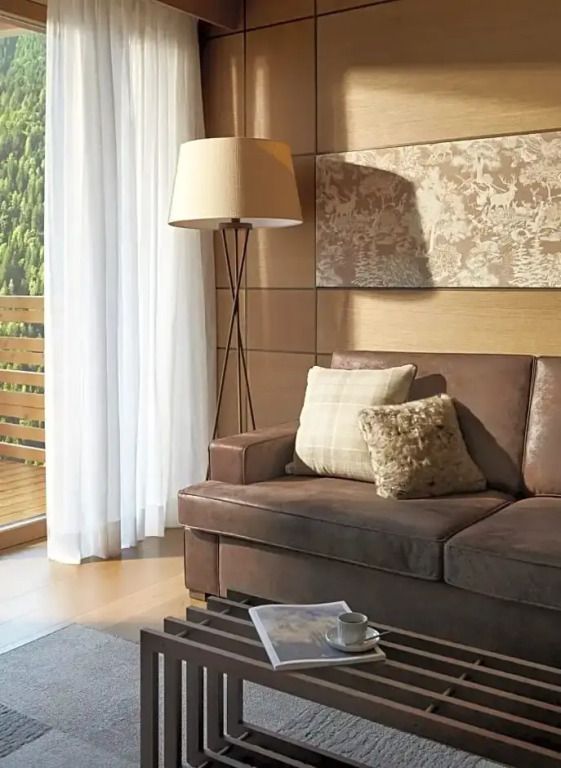 Wohnbereich mit braunem Sofa, Stehlampe und Balkonblick im Lefay Resort Dolomiti