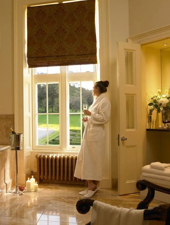 Frau im Bademantel mit Sektglas am Fenster mit Blick auf den Garten