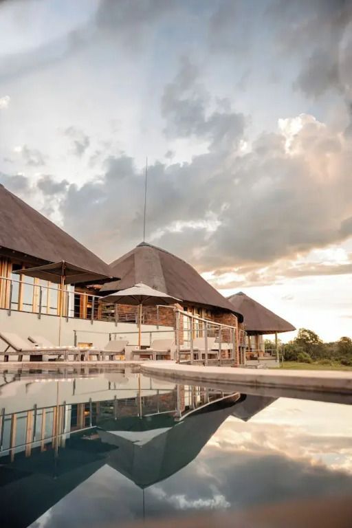 Außenansicht der Villa mit Reetdach und Pool im Vordergrund unter bewölktem Himmel