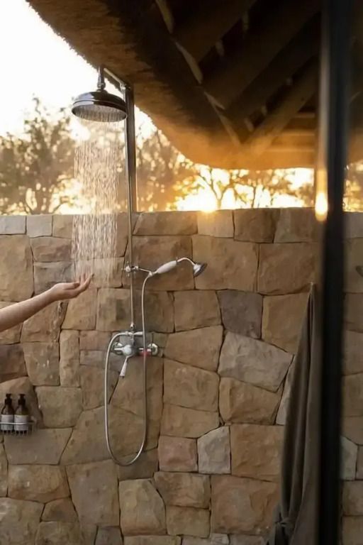 Dusche im Freien mit Natursteinwand und Sonnenuntergang im Hintergrund.