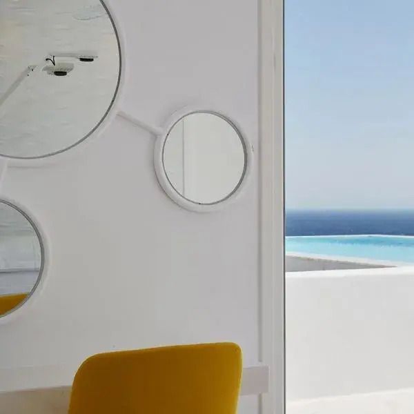 Zimmerdetail mit gelbem Stuhl und runden Spiegeln im Myconian Ambassador Hotel