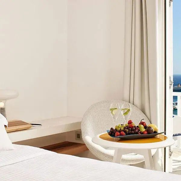 Helles Doppelzimmer mit Meerblick und Balkon, Obstplatte und zwei Weingläser.
